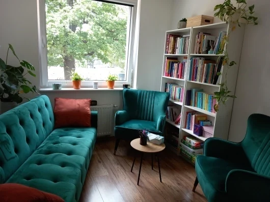 Wnętrze gabinetu PsychoSENS: turkusowa sofa, fotele i regał z książkami